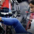 a woman sits in a chair and draws a bow with her foot and mouth